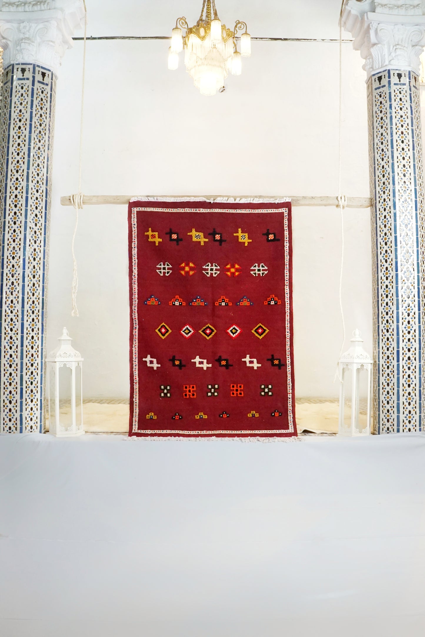 Red patterned rug on a white floor with decorative columns and lights in the background