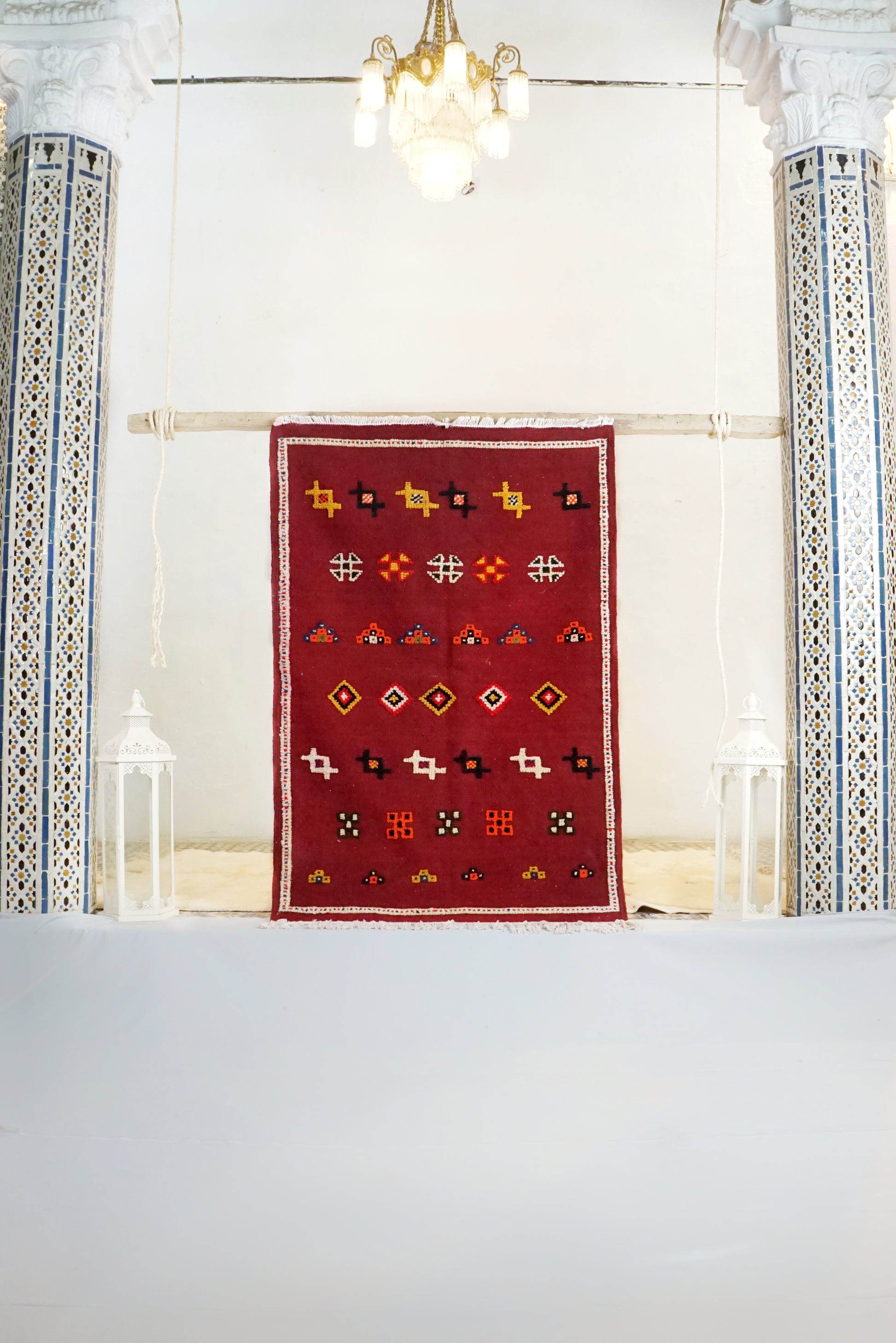 Red patterned rug on a white floor with decorative columns and lights in the background